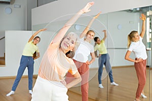 Positive woman doing aerobics exercises with group of people in dance center