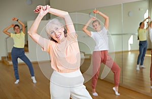 Positive woman doing aerobics exercises with group of people in dance center