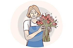 Positive woman flower seller stands with luxurious bouquet and smiling looks at camera