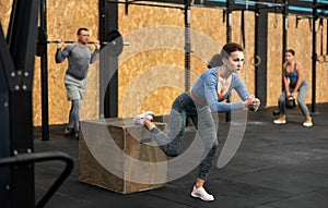 Positive woman with group sports people doing box jump exercise at crossfit gym