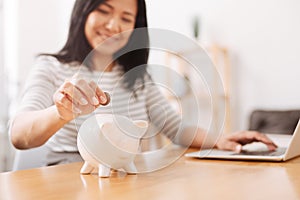 Positive woman putting coins into piggy bank