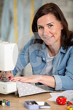 positive woman sewing with professional machine at workshop