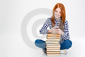 Positive woman sitting near stack of books and using cellphone