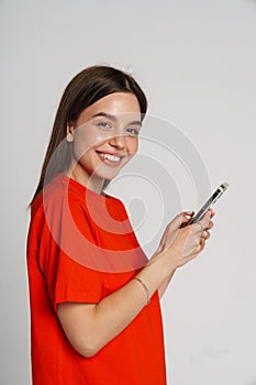 Positive woman smiling while using smartphone isolated over white background