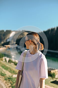 Positive woman standing in the mountains at the resort on a sunny summer day while walking and looking away. Vertical