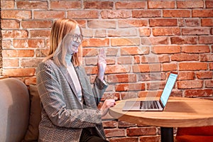 Positive woman student talking, waving hand, using laptop computer video conference while sitting at table in outdoor