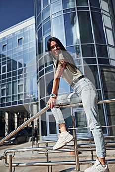 Positive woman with tattoo on arm have fun outdoors against business building at sunny daytime