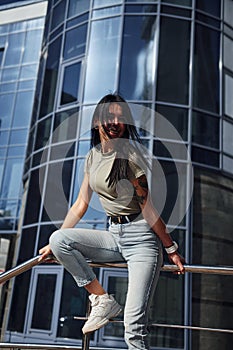 Positive woman with tattoo on arm have fun outdoors against business building at sunny daytime