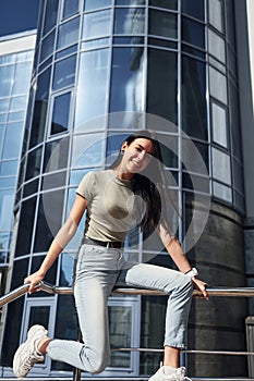 Positive woman with tattoo on arm have fun outdoors against business building at sunny daytime