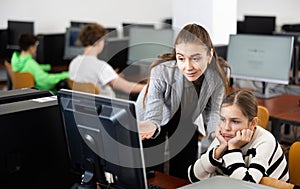 Positive woman teacher together with the girl teaches how to work on computer