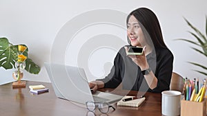 Positive woman using laptop computer and having conversation on mobile phone.