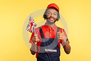 Positive workman holding British flag and showing thumbs up, having satisfied expression.