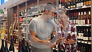 Positive young adult couple looking for perfect wine for solemn occasion in supermarket wine department