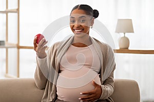 Positive young african american expecting woman holding apple