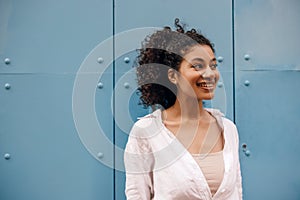 Positive young african woman looks away with smile, posing at camera on blue background.