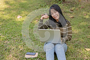 A positive young Asian female college student working remotely at a campus park