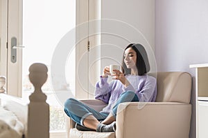 Positive young attractive ethnicity woman in her room holding and enjoying a cup of coffee. thinking positive in