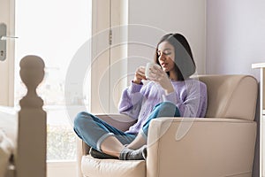 Positive young attractive ethnicity woman in her room holding and enjoying a cup of tea. thinking positive in lockdown