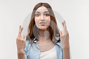 Positive young brunette crossed fingers, waits for good news. Studio shot white background. Facial expression concept