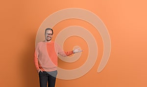 Positive young businessman smiling and presenting new product on empty palm over orange background