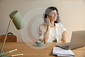 Positive young caucasian girl laughing with eyes closed, using headphones and laptop sitting at desk