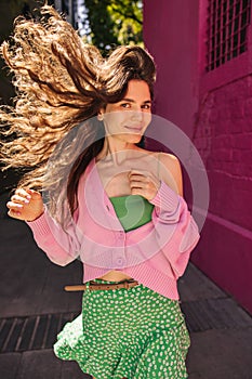 Positive young caucasian woman looking at camera wavying her hair outdoor in sunny weather.