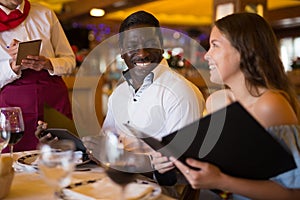 Positive young couple making order at restaurant