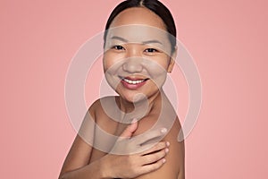 Positive young ethnic lady touching shoulder and smiling in studio