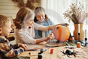 Smiling mother with children creating jack-o-lantern during Halloween celebration at home