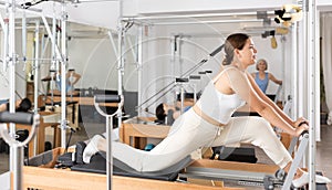 Positive young female in sportswear training twist rotation while using pilates performer bed in gym