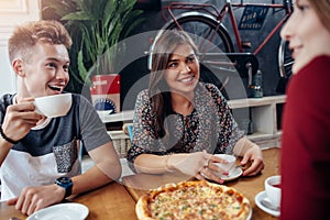 Positive young friends having a lunch break at stylish retro cafe. Boy and girls having a great time together, talking