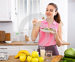 Positive young girl eating vegetable salad in home kitchen