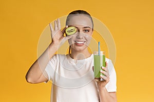 Positive young girl holding kiwi fruit and glass of fresh juice