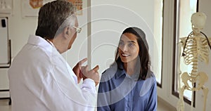 Positive young Hispanic woman talking to senior Indian doctor