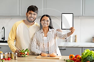 Positive young indian couple cooking at home, showing digital tablet