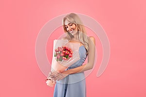 Positive young lady holding lovely tulips on pink studio background. Fun spring holiday concept