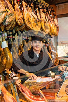 Positive young man carving jamon slices from pig& x27;s leg