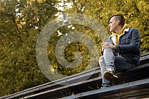 Positive young man with dreadlocks looking away, smiling, sitting on old shabby bench of street bleacher in golden