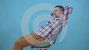 Positive young man with glasses sitting on an orthopedic pillow from hemorrhoids on a blue background