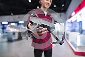 positive young man with a quadcopter in his hands is in the drones store. Buy a dron at an electronics store