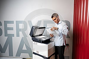 Positive young man using printer in the modern office