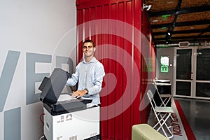 Positive young man using printer in the modern office