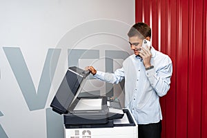 Positive young man using printer in the modern office