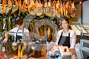Positive young man and woman selling spanish jamon at counter