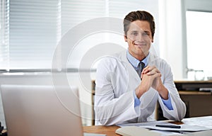 Positive young medical professional. Portrait of a smiling doctor sitting at his desk.