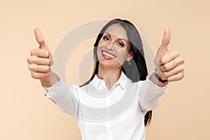 Positive young modern business woman showing thumbs up over beige background. Success and winner concept.