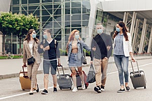 Positive young people in protective masks with luggage outdoor near the airport. Young students return home