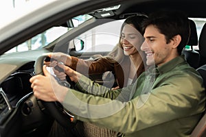 Positive young spouses buying new car, sitting inside modern auto, going on test drive at dealership, free space