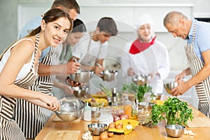 Positive young woman attendee of cooking course learning how to mix sauce