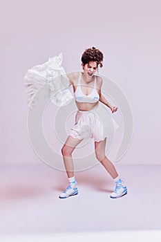 Positive young woman in beautiful sleepwear dancing with white pillow against pink background. Good sleep and energy